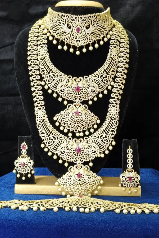 American diamond bridal jewellery set on a display stand — choker, long haram, jhumka and oddiyanam, with gold-toned settings