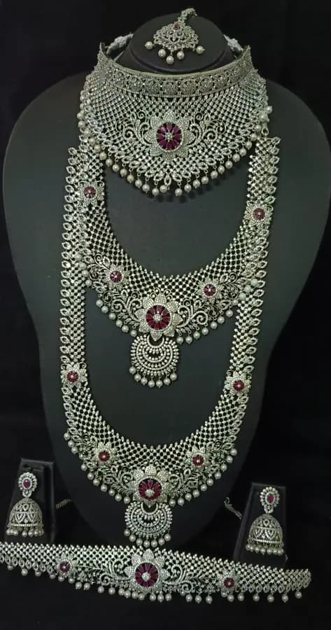American diamond bridal jewellery set on a display stand — choker, layered haram, jhumka and oddiyanam, with red centre stones