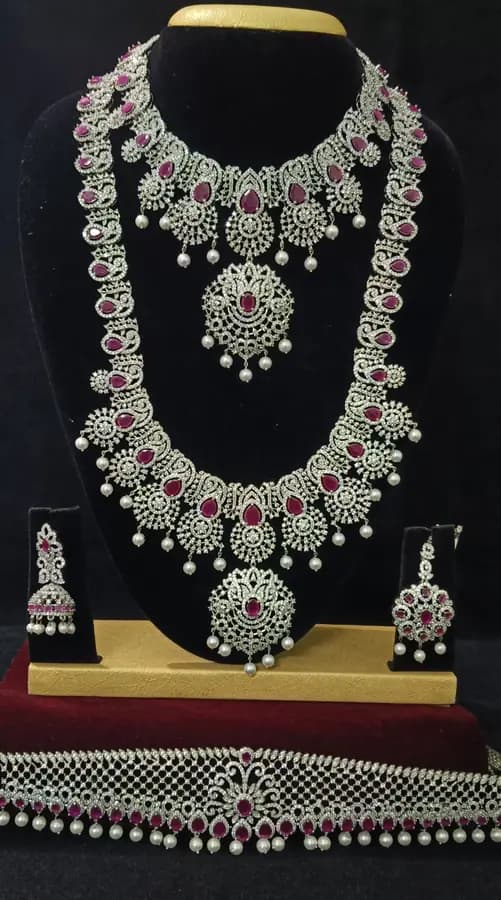 American diamond bridal jewellery set on a display stand — choker, long haram, jhumka and oddiyanam, with red stones