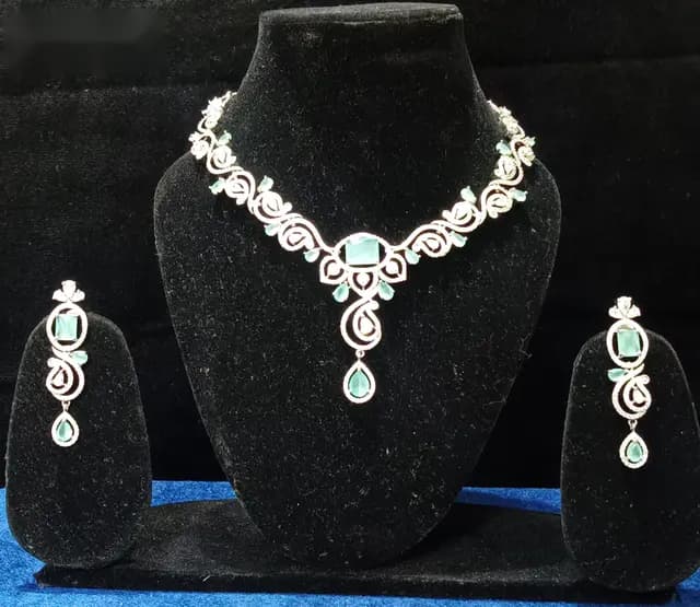 Stone-set bridal choker and earrings on a display stand — a necklace with matching earrings, with a green centre stone