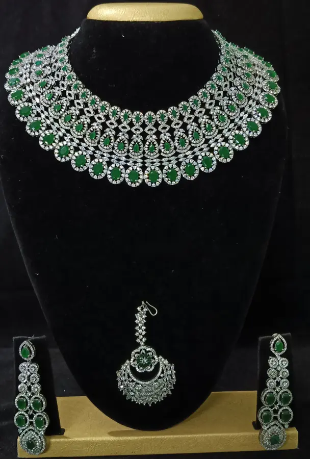 Stone-set bridal choker and earrings on a display stand — a wide choker with matching earrings and maang tikka, with green stones