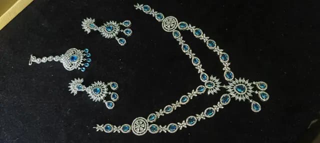Stone-set bridal choker and earrings on a display stand — a necklace with matching earrings and maang tikka laid flat, with green stones
