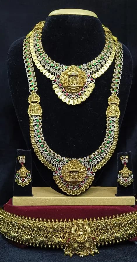 Antique gold temple jewellery bridal set on a display stand — short necklace, long haram, jhumka and oddiyanam, with green and white stones