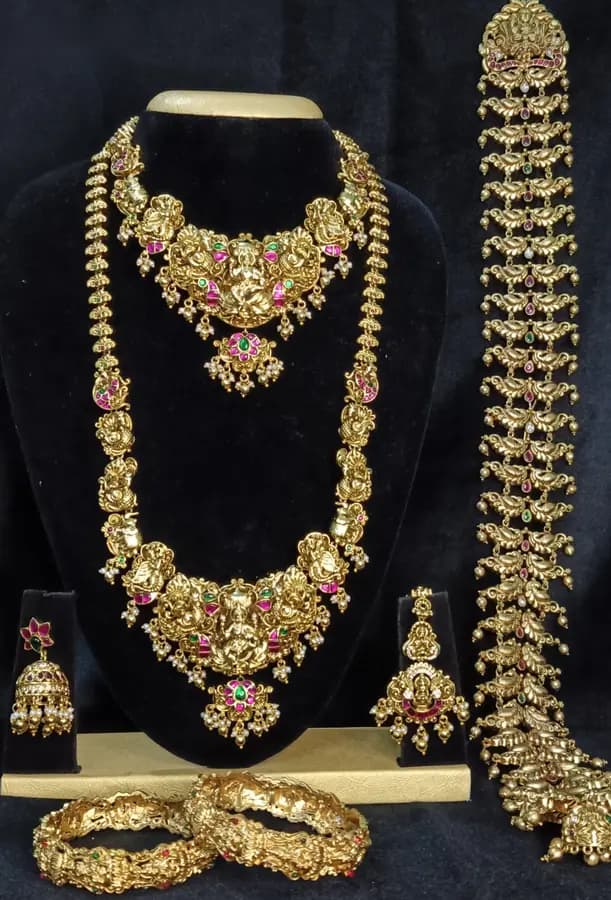 Antique gold temple jewellery bridal set on a display stand — necklace, long haram, jhumka, bangles and a hair ornament