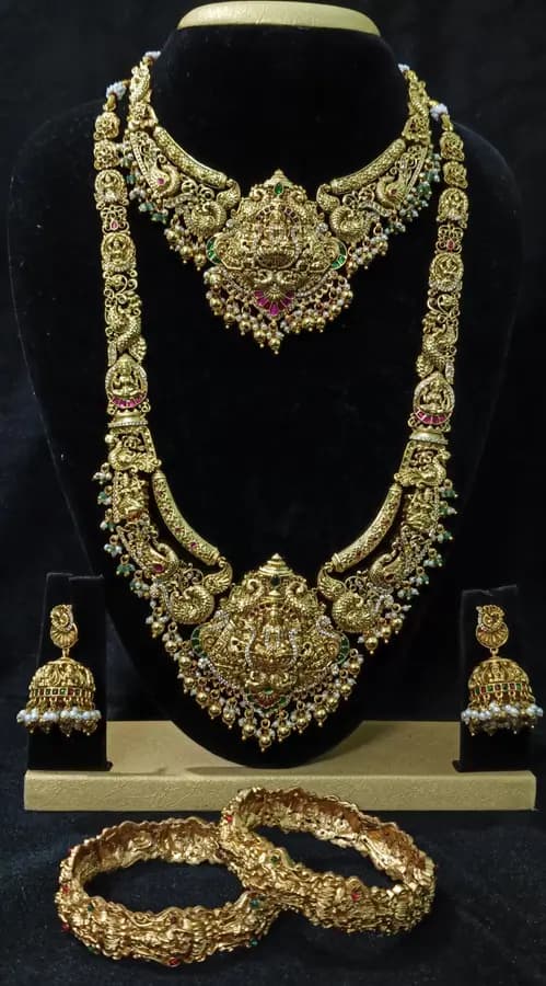 Antique gold temple jewellery bridal set on a display stand — short necklace, long haram, jhumka and bangles, with red stone accents