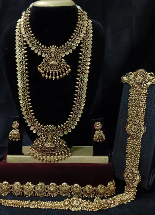 Antique gold temple jewellery bridal set on a display stand — short necklace, long haram, jhumka, oddiyanam and a vanki