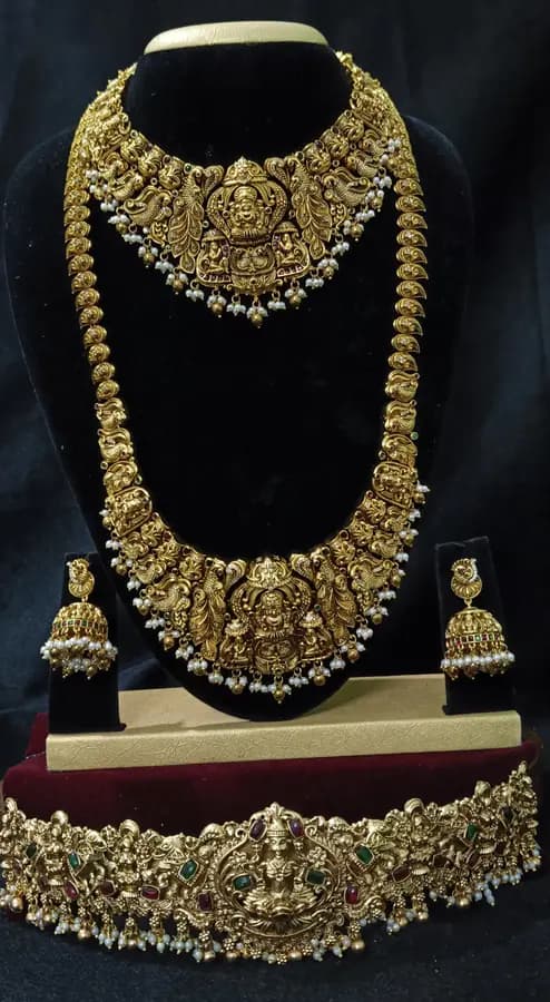 Antique gold temple jewellery bridal set on a display stand — short necklace, long haram, jhumka and oddiyanam