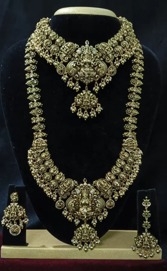 Antique gold temple jewellery bridal set on a display stand — short necklace, long haram and jhumka, with dense gold work