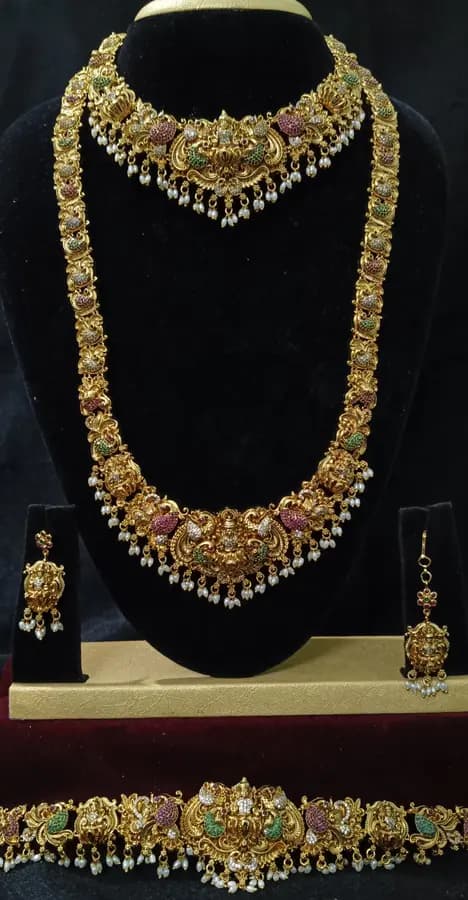 Antique gold temple jewellery bridal set on a display stand — short necklace, long haram, jhumka and oddiyanam