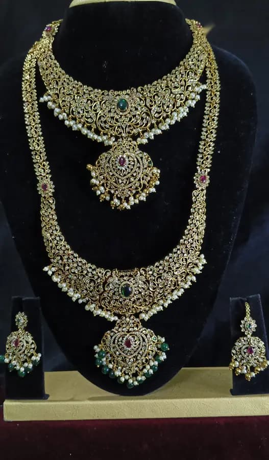 Antique gold temple jewellery bridal set on a display stand — short necklace, long haram and jhumka, with a green centre stone