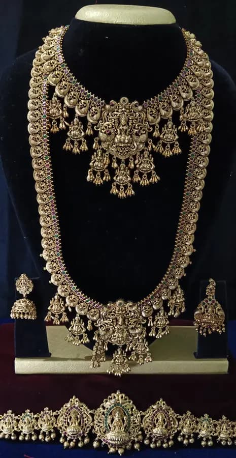 Antique gold temple jewellery bridal set on a display stand — short necklace, long haram, jhumka and oddiyanam, with dense gold work