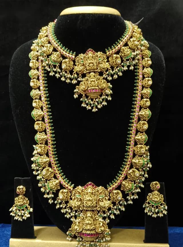 Antique gold temple jewellery bridal set on a display stand — necklace, large mango haram and jhumka, with a red pendant