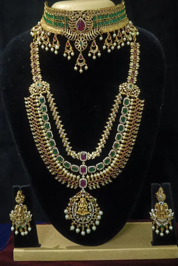 Antique gold temple jewellery bridal set on a display stand — choker, long haram and jhumka, with green stones