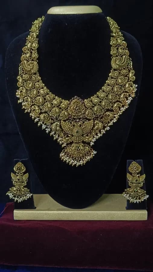 Antique gold temple jewellery bridal set on a display stand — a single short necklace and jhumka, with Lakshmi motifs