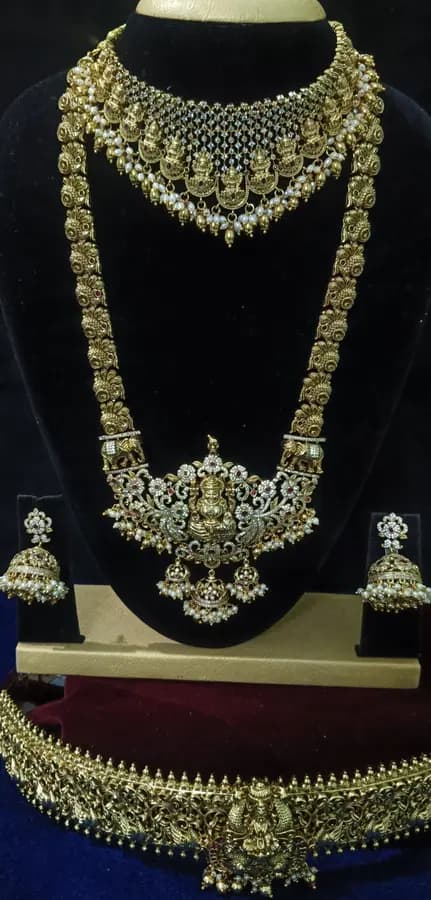 Antique gold temple jewellery bridal set on a display stand — short necklace, long haram, jhumka and oddiyanam