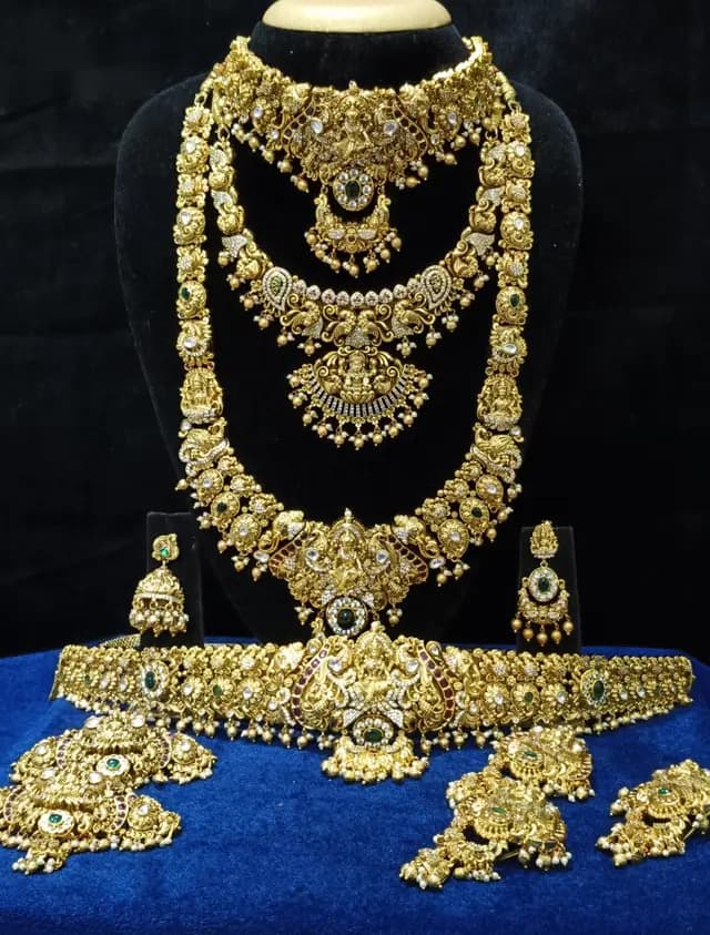 Antique gold temple jewellery bridal set on a display stand — short necklace, long haram, jhumka and oddiyanam