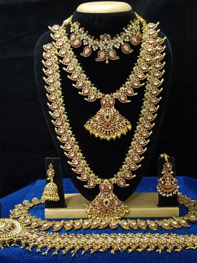 Antique gold temple jewellery bridal set on a display stand — choker, long haram, jhumka and oddiyanam, with red stones