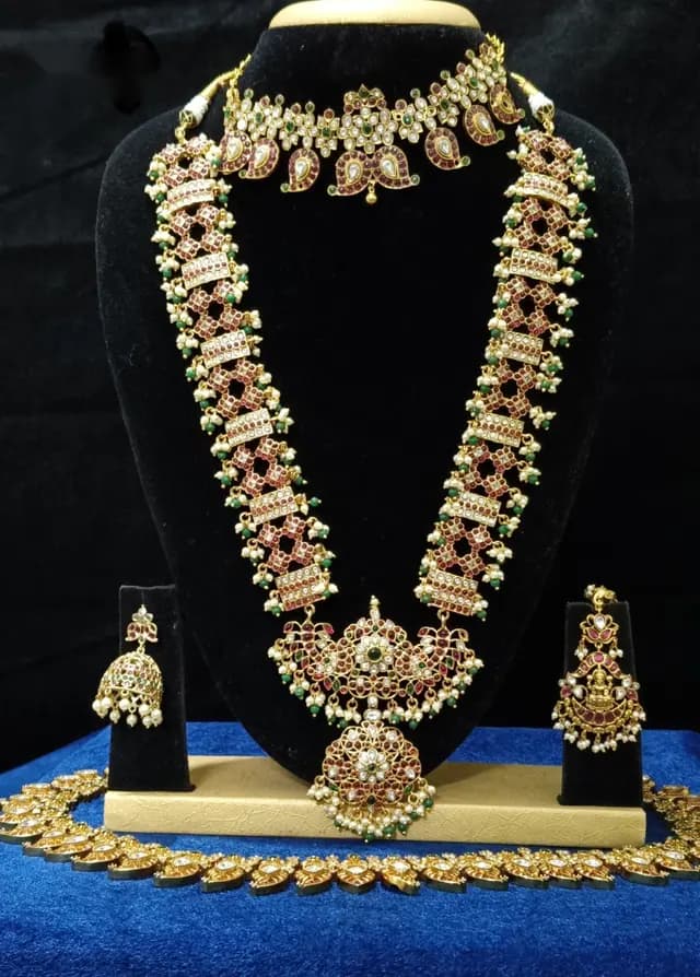 Antique gold temple jewellery bridal set on a display stand — short necklace, long haram, jhumka and oddiyanam, with red stones