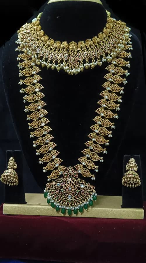 Antique gold temple jewellery bridal set on a display stand — short necklace, long haram and jhumka, with green drops