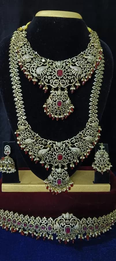 Antique gold temple jewellery bridal set on a display stand — short necklace, long haram, jhumka and oddiyanam, with pale silver-toned stones