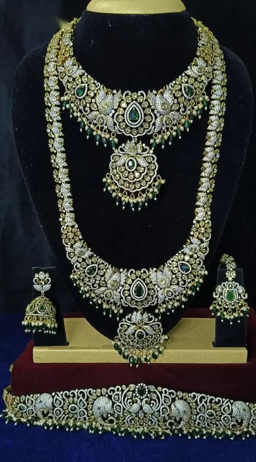 Antique gold temple jewellery bridal set on a display stand — short necklace, long haram, jhumka and oddiyanam, with pale stones and green drops